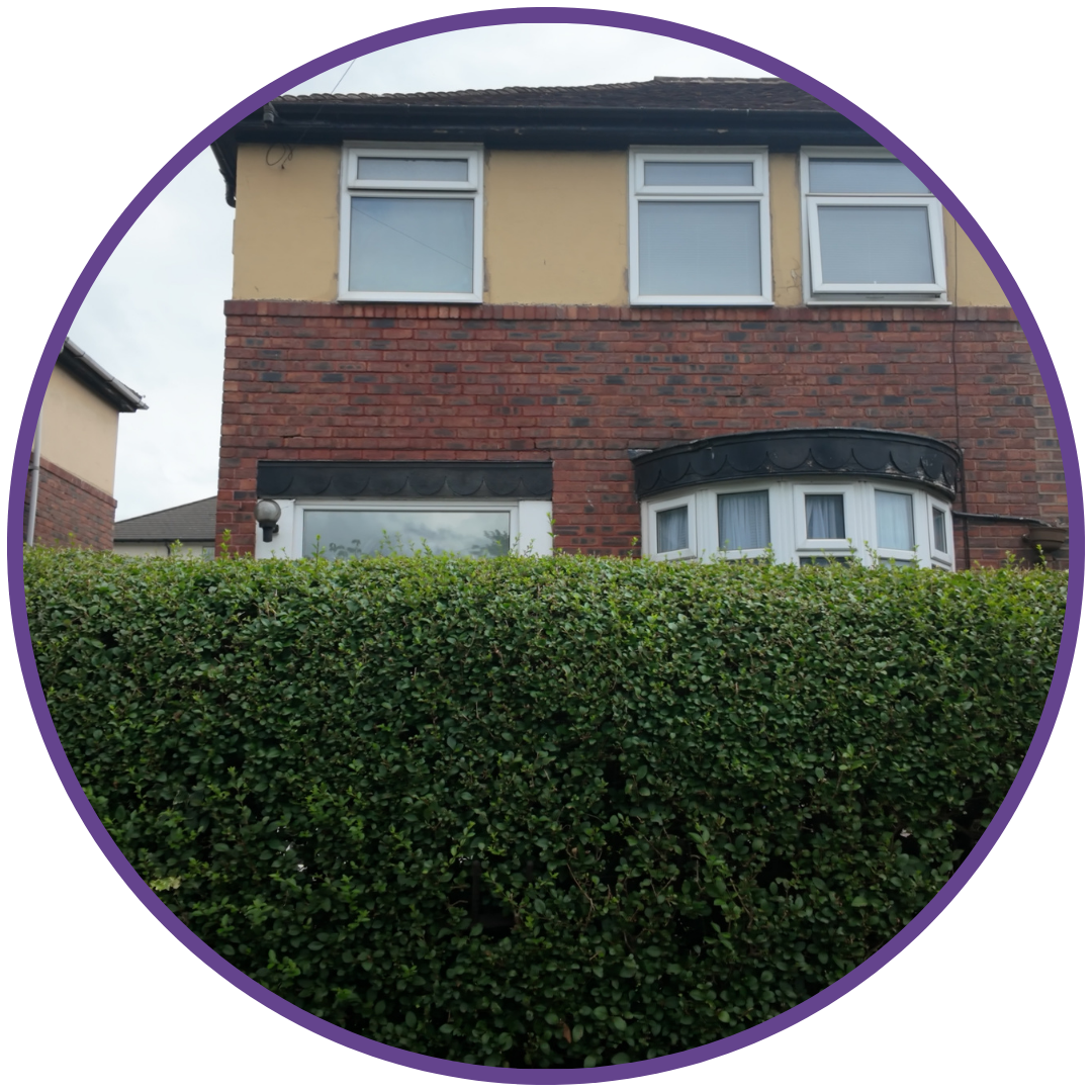 Trauma Project Website Paegs Circle image of a the front view of a house with a tall hedge covering half of the view. The house is painted dark yellow with brown bricks. Located in the United Kingdom.