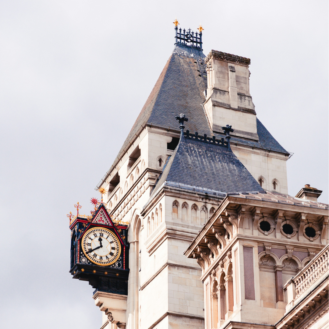 Clock tower on the Royal Courts of Justice building in London, featuring ornate Gothic architecture and a decorative clock face against a cloudy sky.