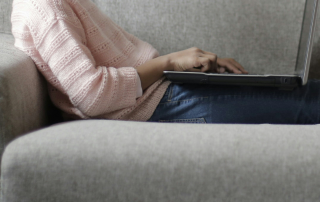 A child sitting on a sofa using a laptop, shown from the shoulders down.