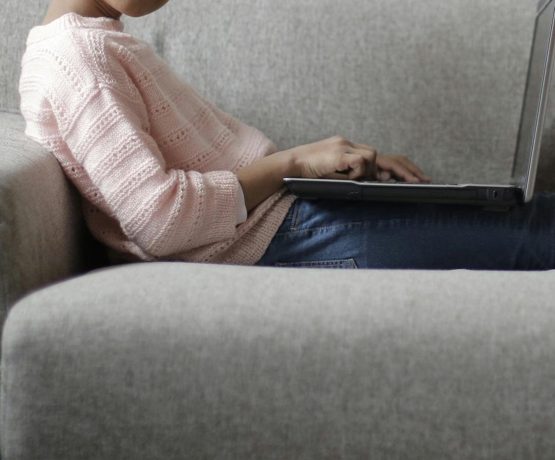 A child sitting on a sofa using a laptop, shown from the shoulders down.